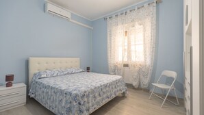 A bedroom with a bed, a chair, a nightstand, and a window with curtains. - This beautiful and spacious apartment in Rio Marina offers all the comforts for your holiday on Elba (Rio Marina)