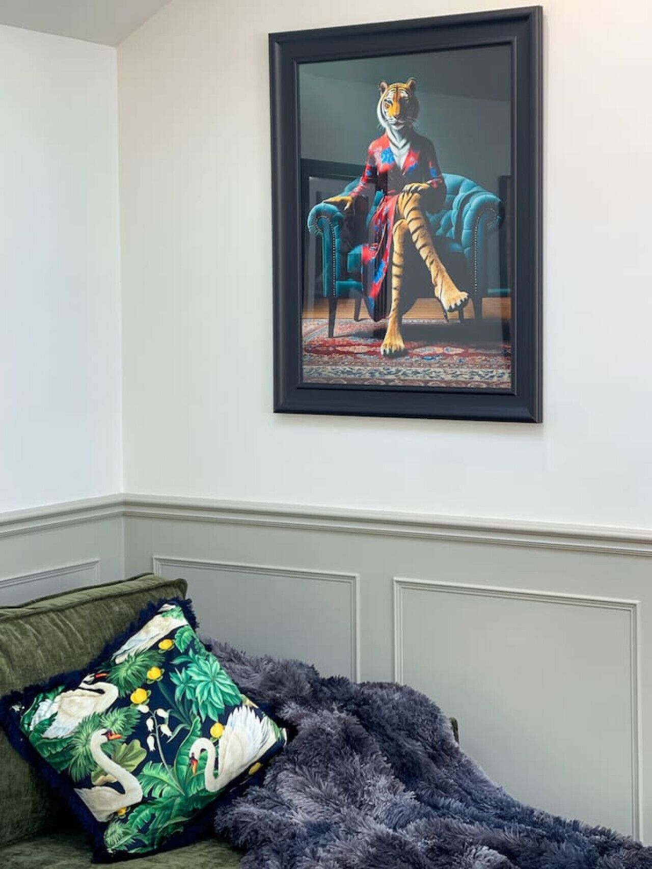 A framed artwork of a tiger in a chair, a plush sofa with a swan pillow, and a patterned throw blanket.