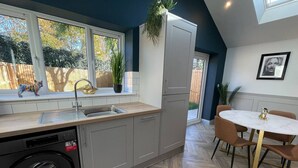 Une cuisine moderne avec des meubles gris, un lave-linge encastré, un évier et un coin repas comprenant une table ronde et des chaises.