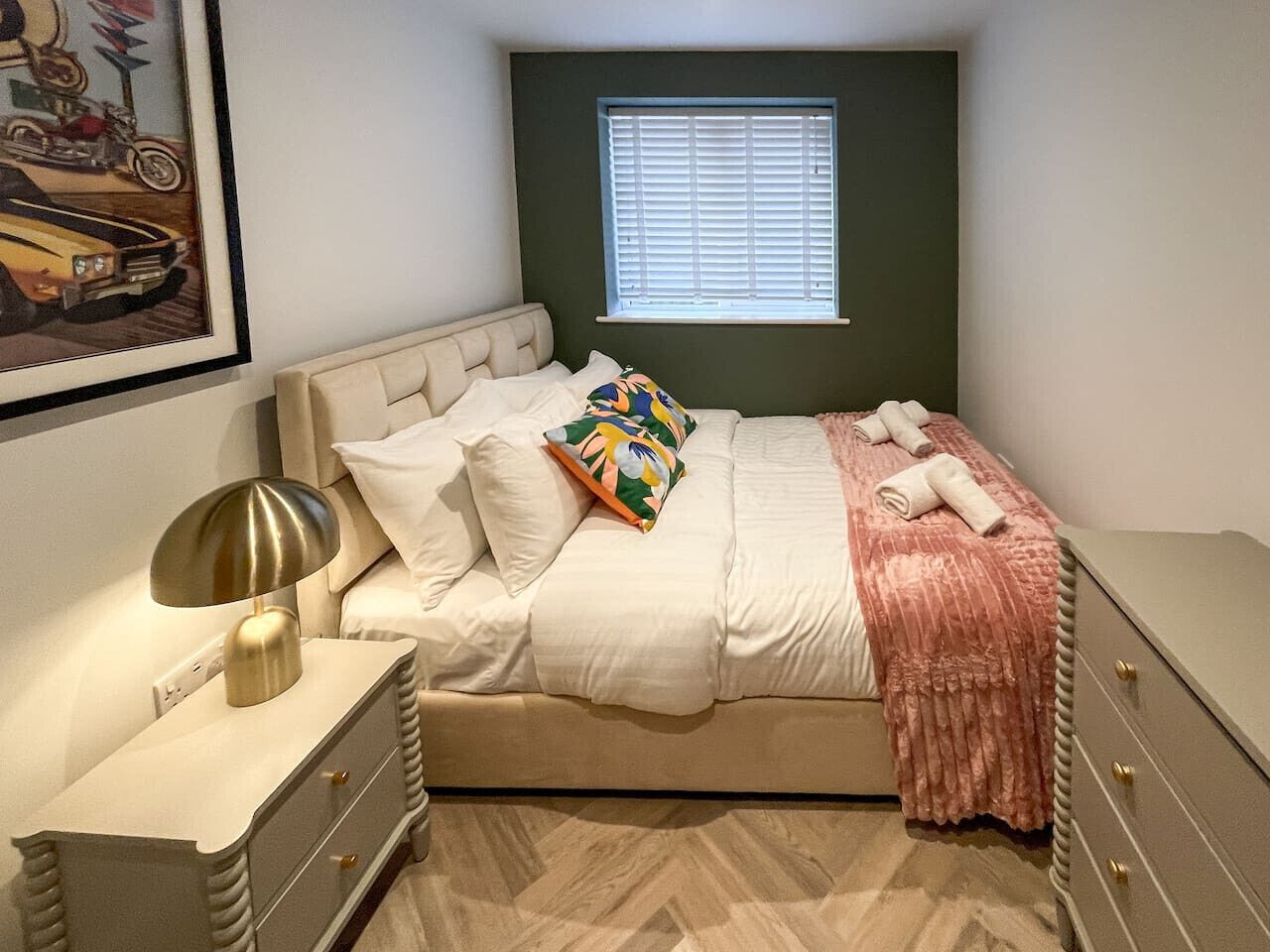 A bedroom with a bed, bedside tables, a lamp, a window, and a framed picture on the wall.