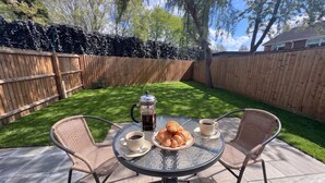 A round glass table with wicker chairs, a coffee pot, croissants, and cups of coffee. - Large New-Build 1 Bed House Near Science Park (Arbury)