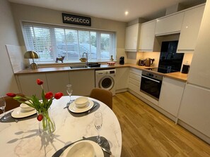 A modern kitchen with white cabinets, a built-in oven, and a window with blinds.