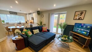A modern living room with a dark blue sectional sofa, a small round side table, and a television on a wooden stand. - Large New-Build 1 Bed House Near Science Park (Arbury)