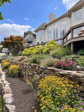 A residential area with stone walls and a variety of colorful flowers. - Hilltop Haven 3BR Lakefront Escape – Private Island, Hot Tub, Kayaks, Pool Table (Rome City)