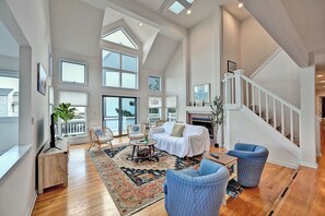 Un salon spacieux avec un haut plafond, de grandes fenêtres, une cheminée et un escalier.