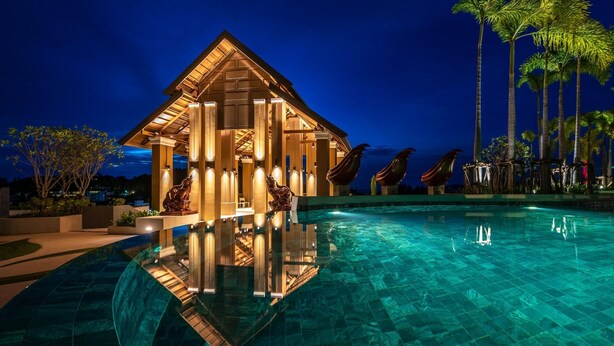 A modern hotel with a pool, palm trees, and a well-lit facade at night.