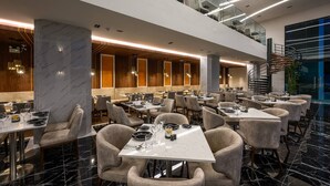 A modern restaurant with multiple dining tables and chairs, a marble floor, and a staircase leading to an upper level.