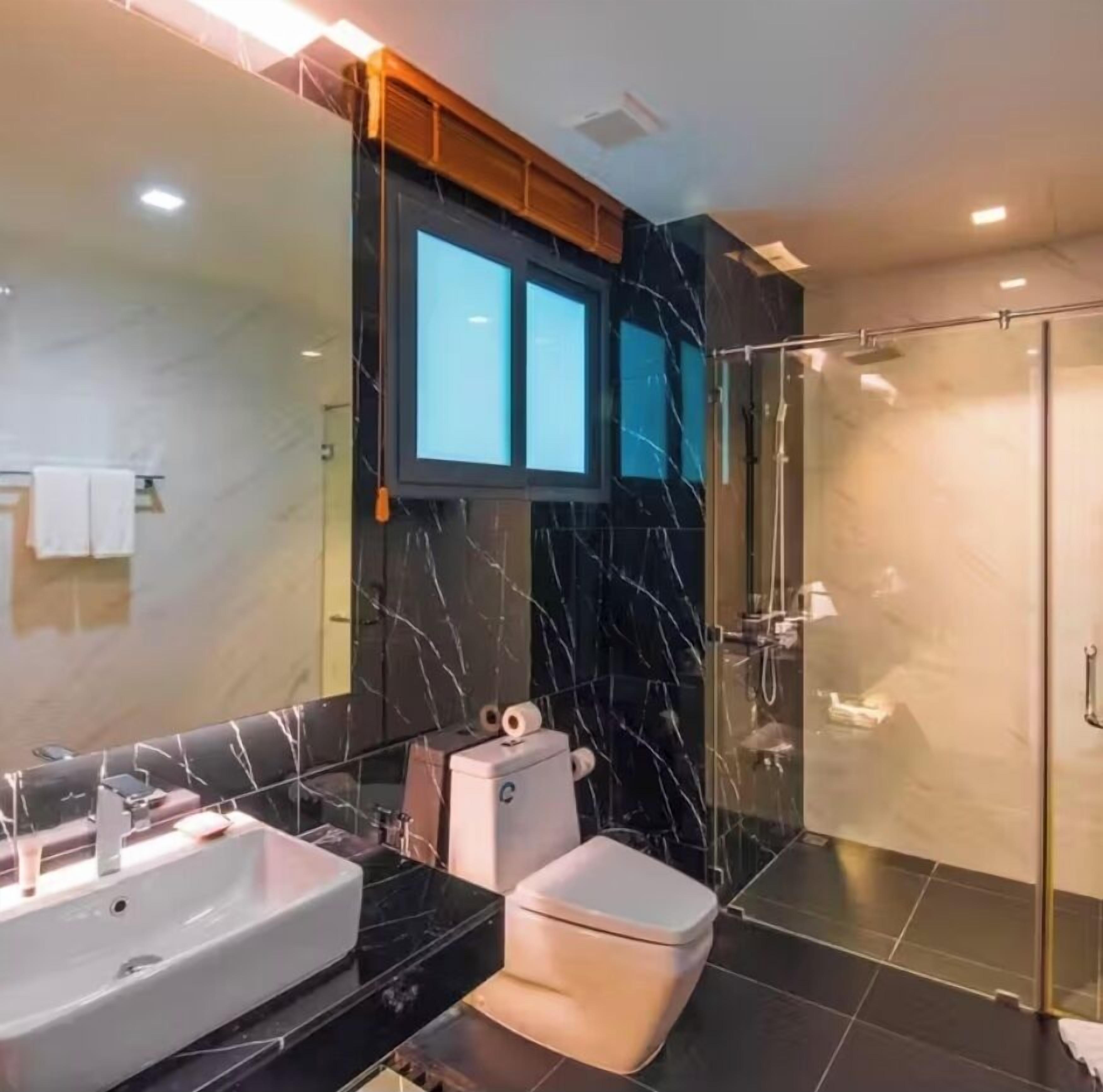 A modern bathroom with a large mirror, a white toilet, a sink, and a glass-enclosed shower.