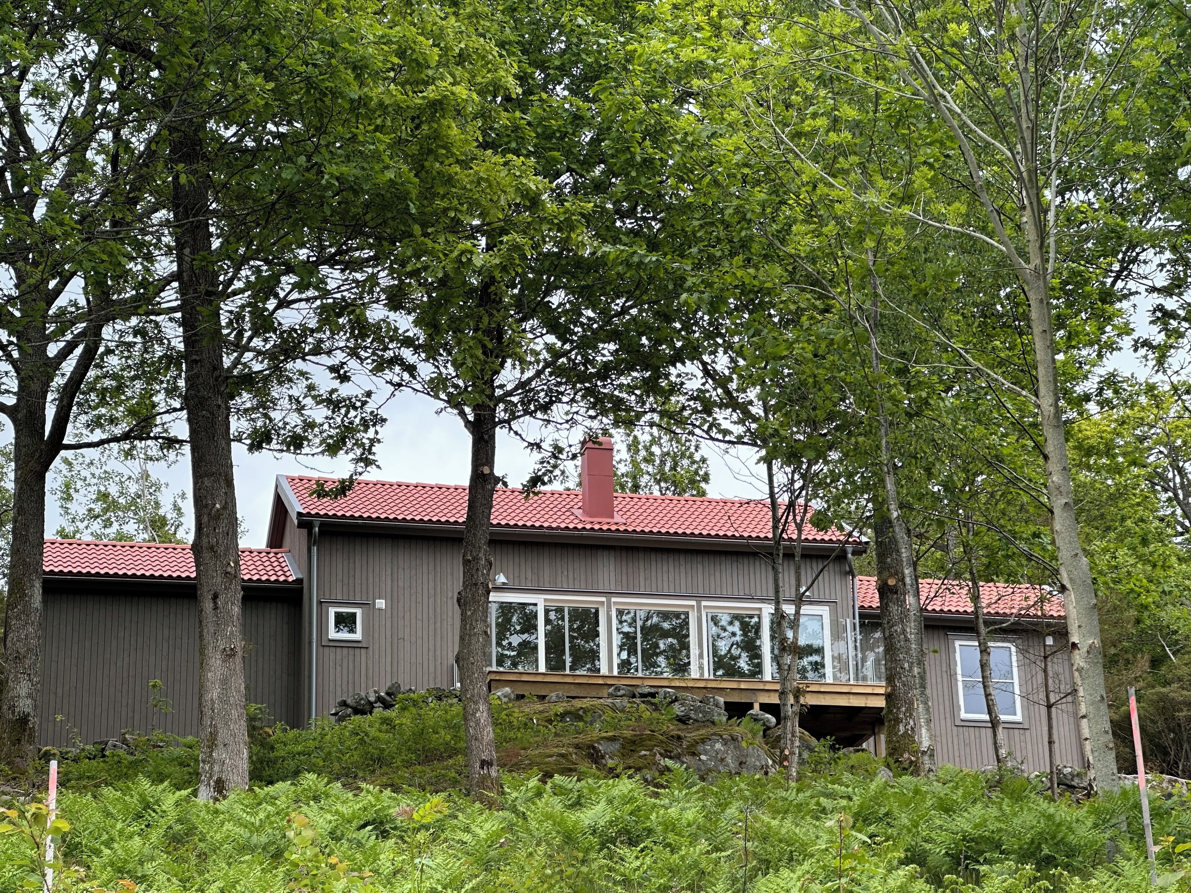 A modern house with a red-tiled roof, surrounded by dense green foliage and trees.