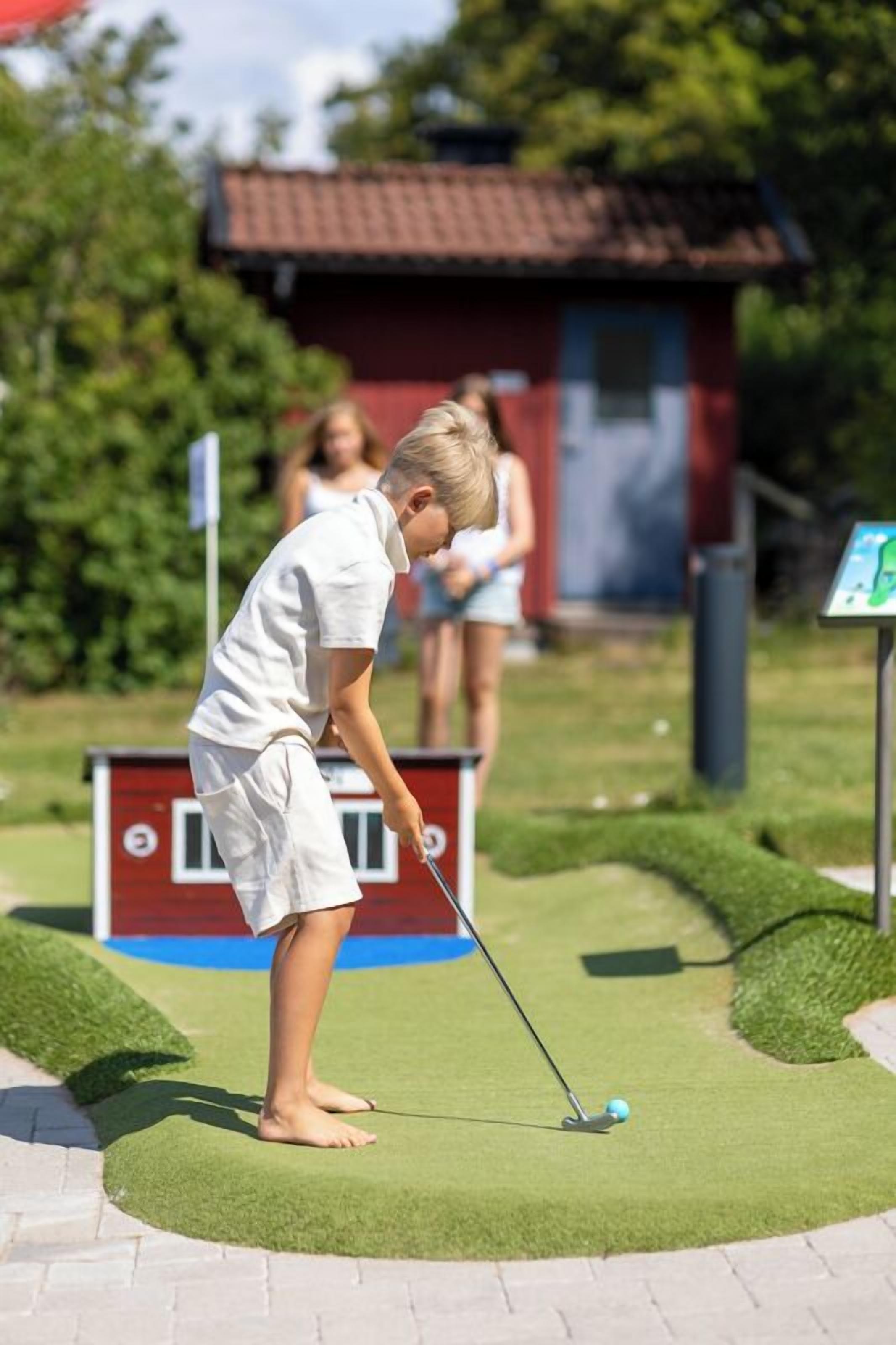 A person playing golf on a green with a red and blue sign in the background.