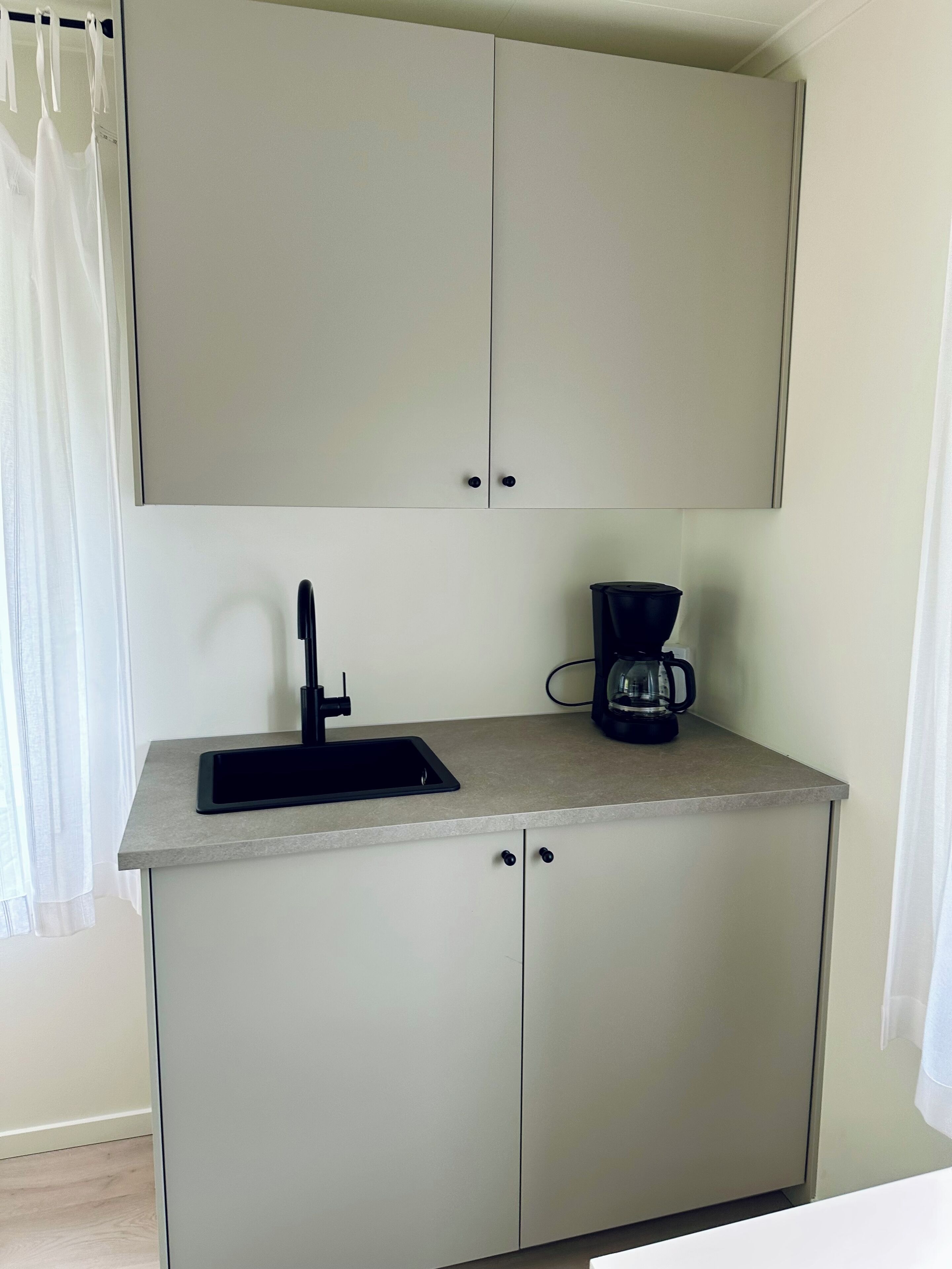 A small kitchenette with a sink, a coffee maker, and cabinets.