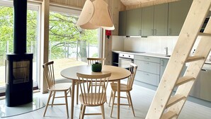 Een moderne keuken met houten kastjes, een ronde eettafel met stoelen en een groot raam met uitzicht op bomen.