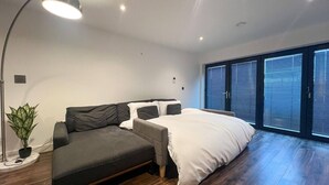 Ein modernes Schlafzimmer mit Schlafsofa, großem Fenster mit Jalousien und einer Topfpflanze.
