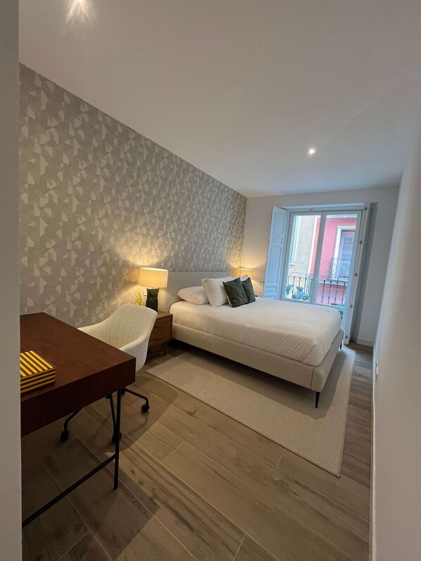 A bedroom with a bed, bedside table, lamp, and a view of the outside balcony.