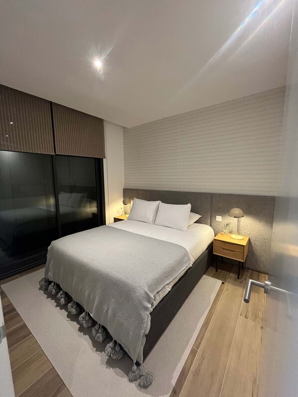 A modern bedroom with a large bed, a nightstand, a lamp, and a sliding door. - w Chic Urban 3BR w Sunny Terrace in Chueca (Madrid)