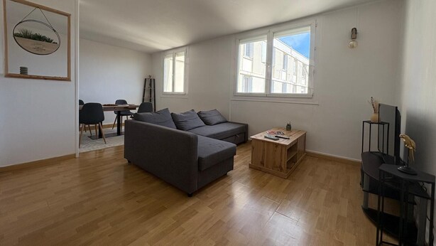 Ein geräumiges Wohnzimmer mit grauem Sofa, einem Holztisch und einem Essbereich mit Tisch und Stühlen.