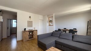 Ein modernes Wohnzimmer mit einem grauen Ecksofa, einem Holztisch und einem Essbereich mit Tisch und Stühlen.
