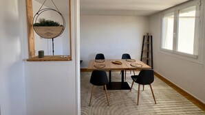 Ein Essbereich mit einem Holztisch, schwarzen Stühlen, einem hängenden Blumentopf und einer an der Wand stehenden Leiter.