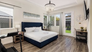 A bedroom with a bed, a desk, a treadmill, a chandelier, and a door leading to a balcony. - Wildflower (Windsor)