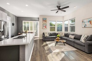 A modern kitchen with a central island, a dining area with a sofa, and a ceiling fan.