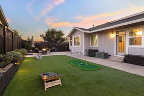 A backyard with a putting green, a pool table, and a barbecue area.