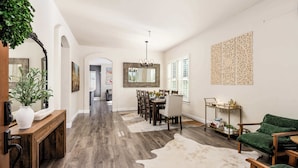 A spacious living area with a dining table, chairs, a green sofa, a wooden console table, and a large mirror. - Wildflower (Windsor)
