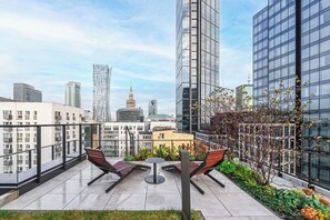Una terraza en la azotea con dos sillones de descanso, una mesita y vistas al horizonte de la ciudad.