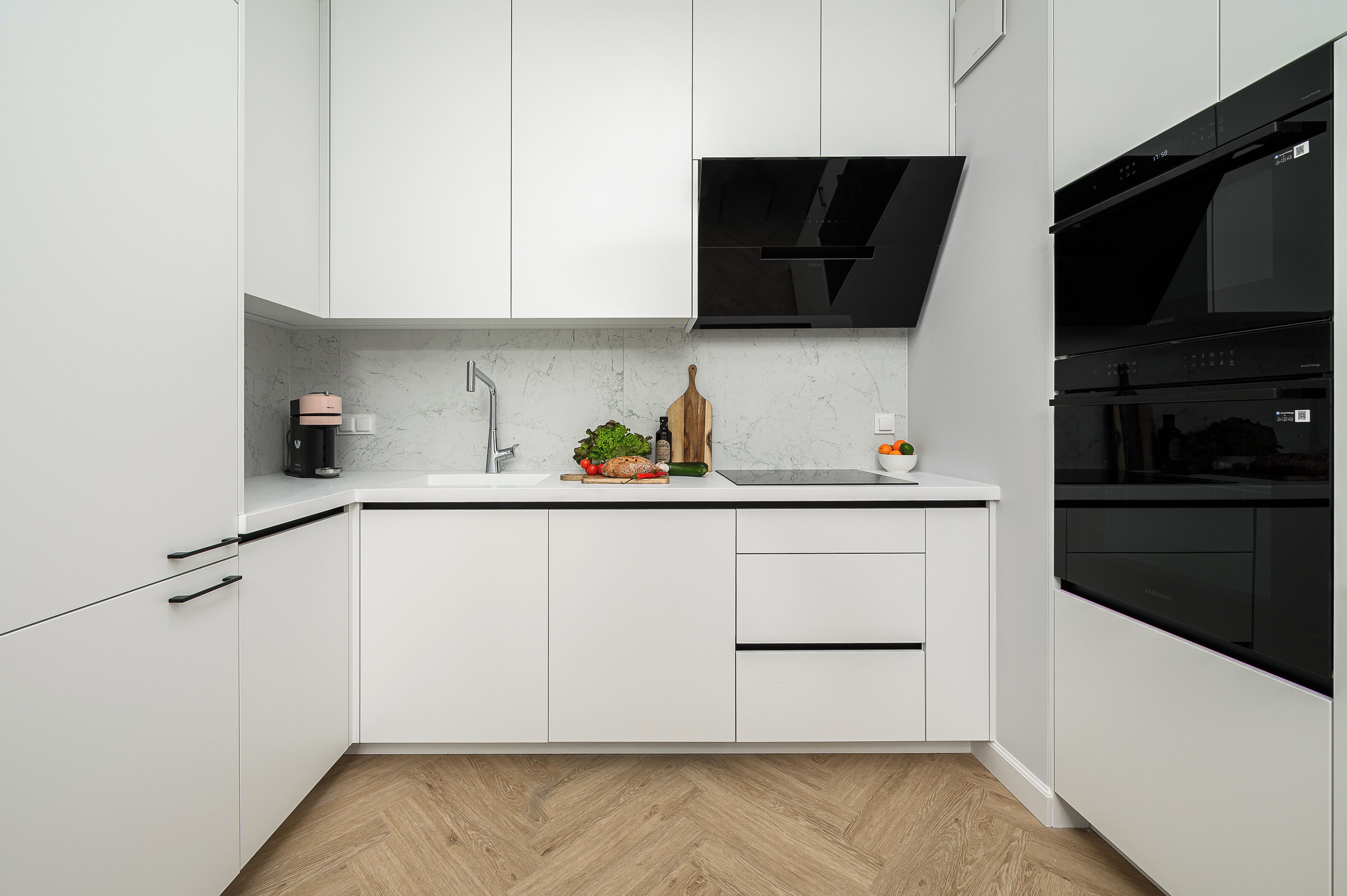 Une cuisine moderne avec des armoires blanches, une hotte noire et un four encastré.