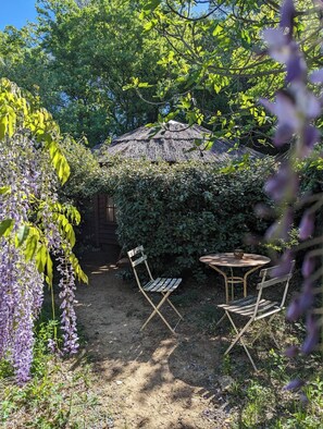A garden with a thatched-roof structure, two wooden chairs, and a small table.