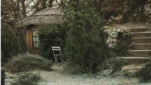 A rustic cabin with a thatched roof, a wooden door, and a small porch. A white folding chair is placed outside. - Yourte in Provence , at la Mauvaise Herbe, Barjols (Barjols)