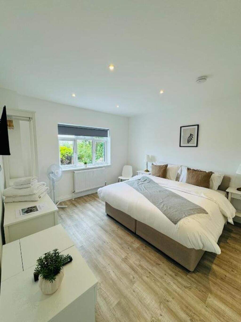A modern bedroom with a large bed, a bedside table, a chair, a window, and a radiator.