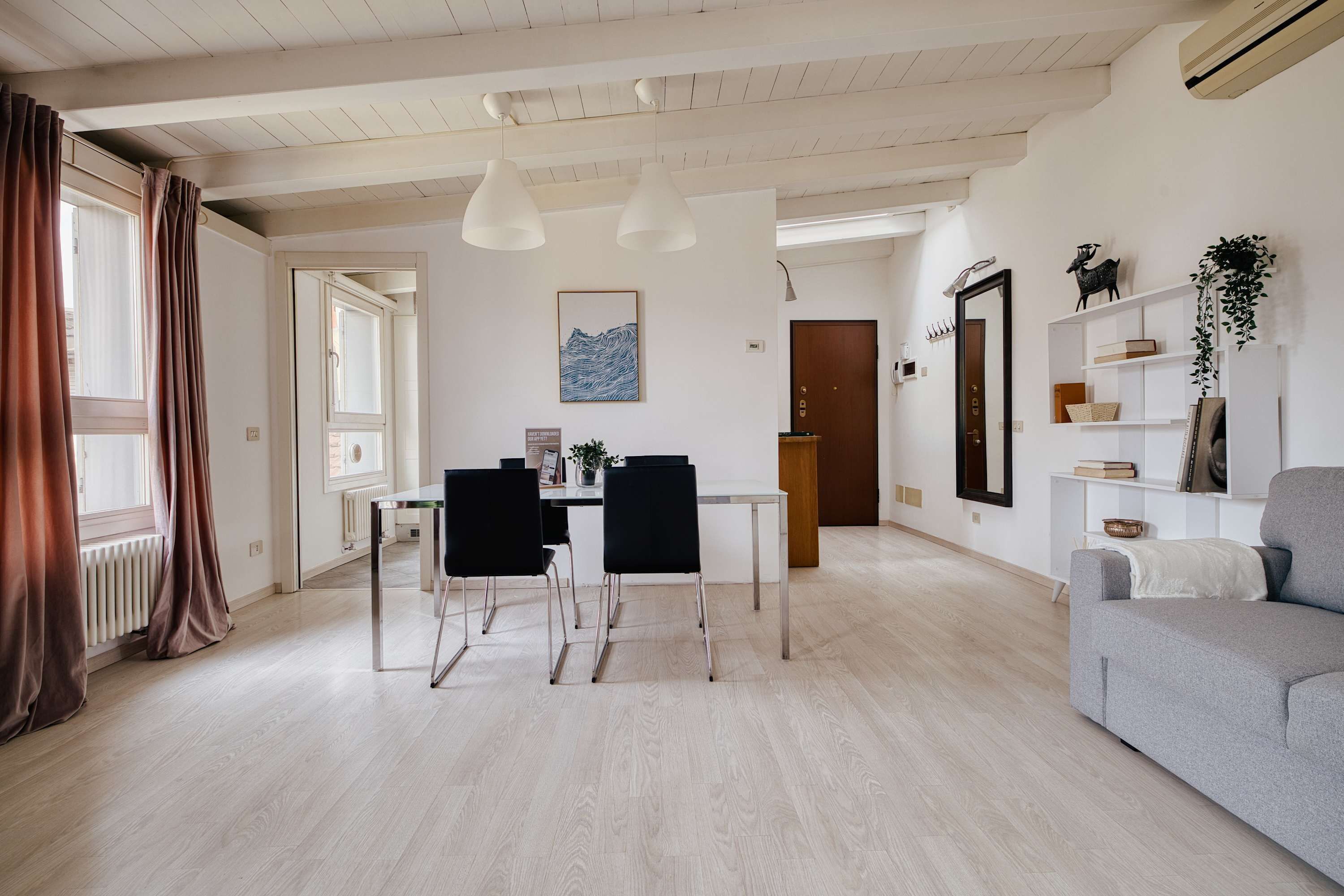 Ein modernes Wohnzimmer mit Essbereich, ausgestattet mit einer Couch, einem Esstisch, Stühlen, Pendelleuchten und einem großen Spiegel.