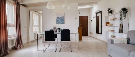 Ein modernes Wohnzimmer mit Essbereich, ausgestattet mit einer Couch, einem Esstisch, Stühlen, Pendelleuchten und einem großen Spiegel.