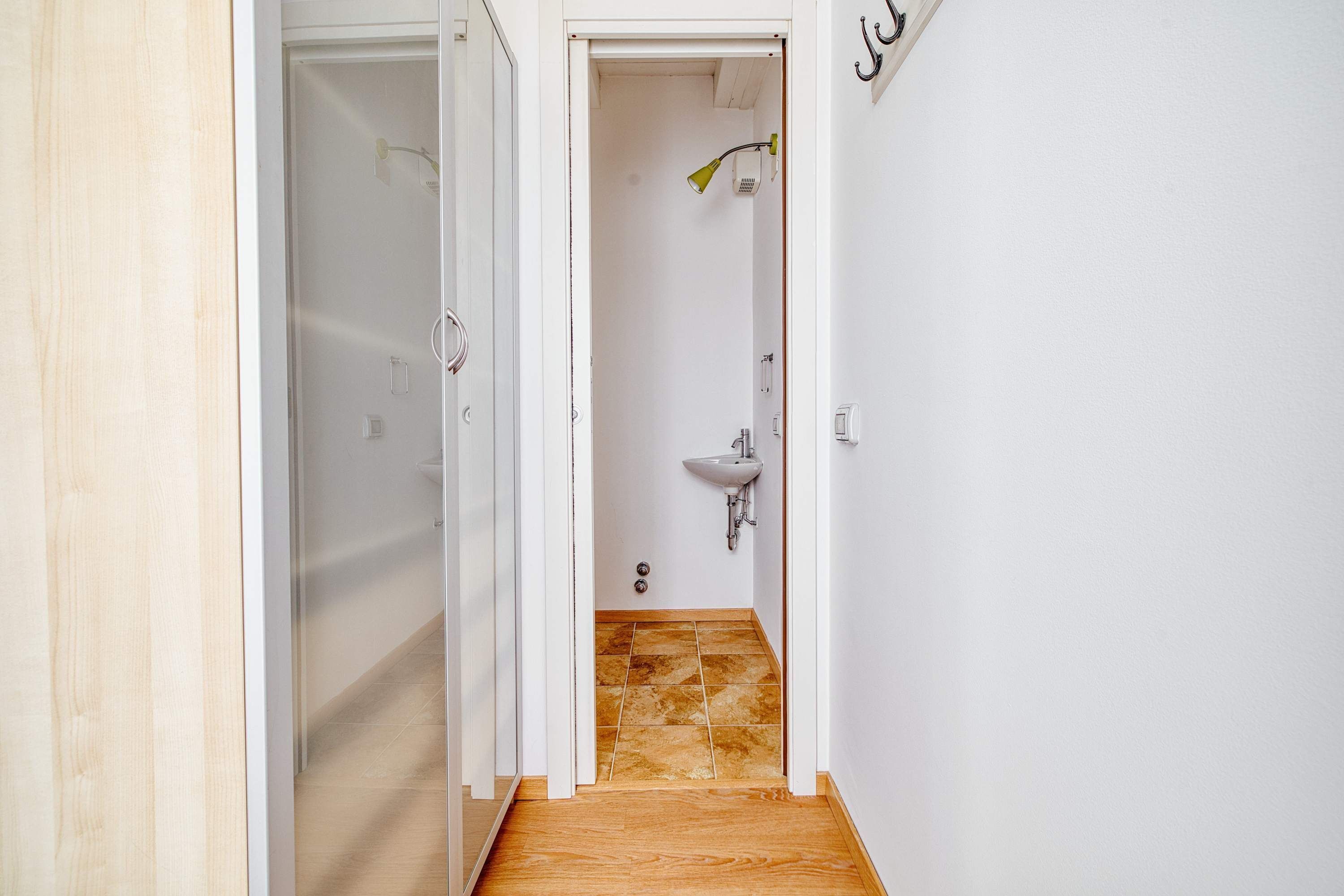 A narrow hallway with a shower area, a sink, and a door leading to another room.