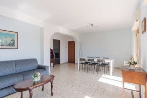 A spacious living room with a grey sofa, a wooden coffee table, and a dining area with a white table and black chairs.