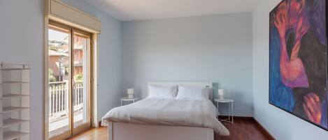 A bedroom with a bed, a nightstand, a wall-mounted painting, a sliding glass door, and a white shelving unit.