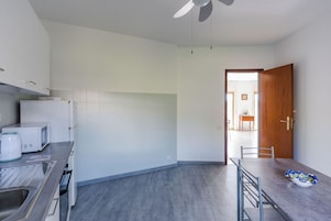 A modern kitchen with white cabinets, a microwave, a kettle, and a dining area with a table and chairs.