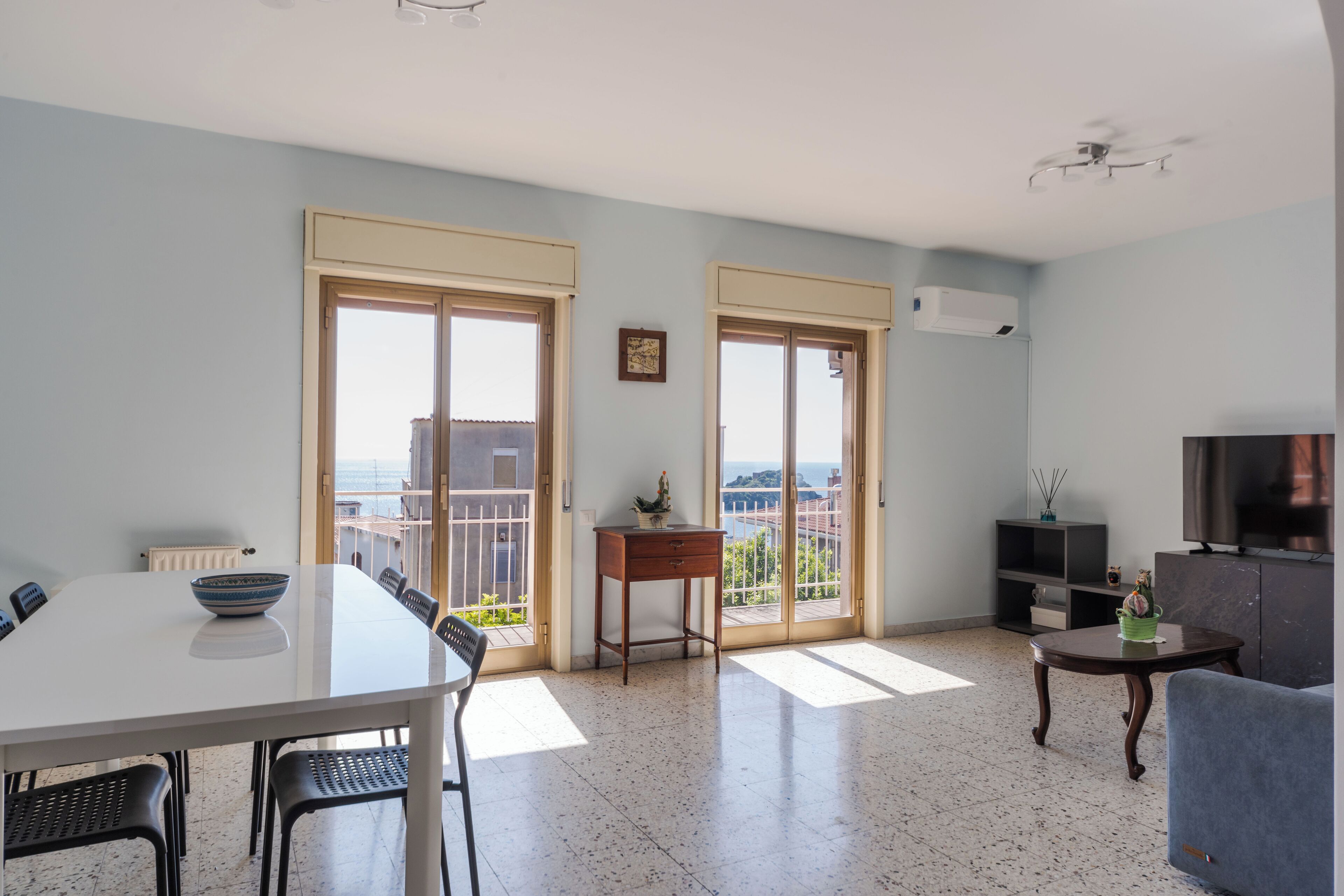 Een ruime woonkamer met een eettafel, stoelen, een bank, een televisie en een balkon met uitzicht.