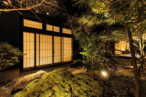 Ein traditionelles japanisches Gebäude mit großen Schiebetüren, umgeben von einem Garten mit Steinen und Pflanzen.
