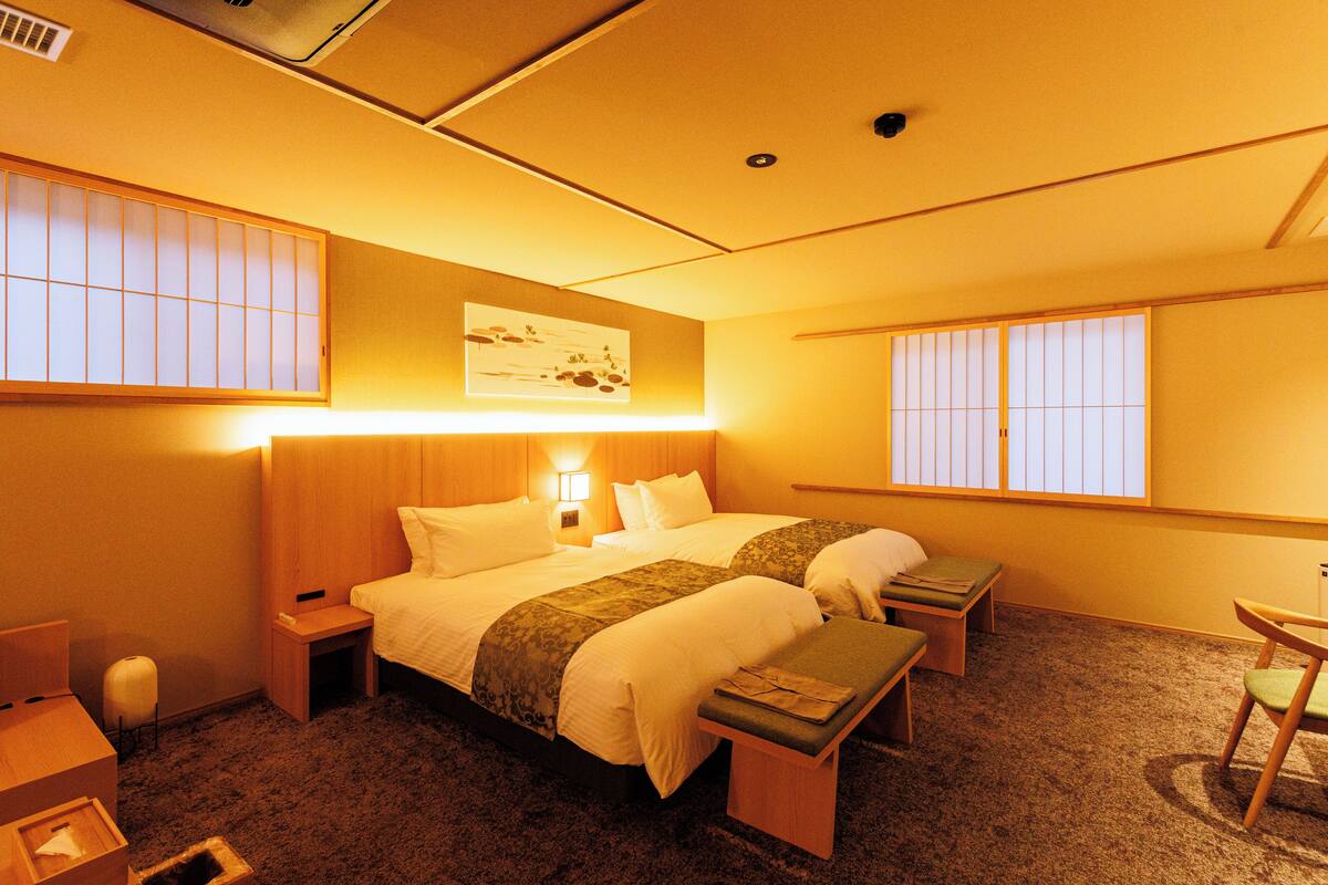 A hotel room with two beds, a bedside table, a chair, and a small table.