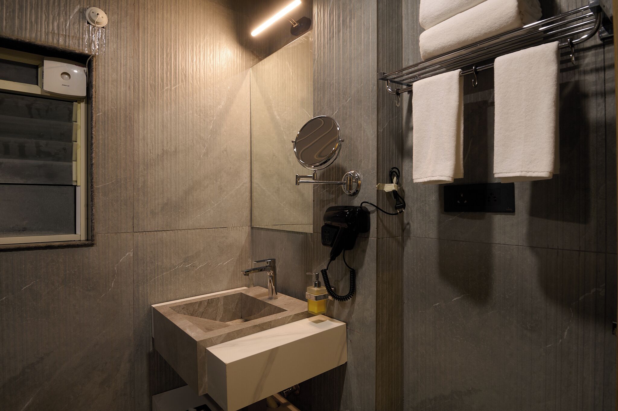 A modern bathroom with a sink, mirror, towel rack, and hairdryer.