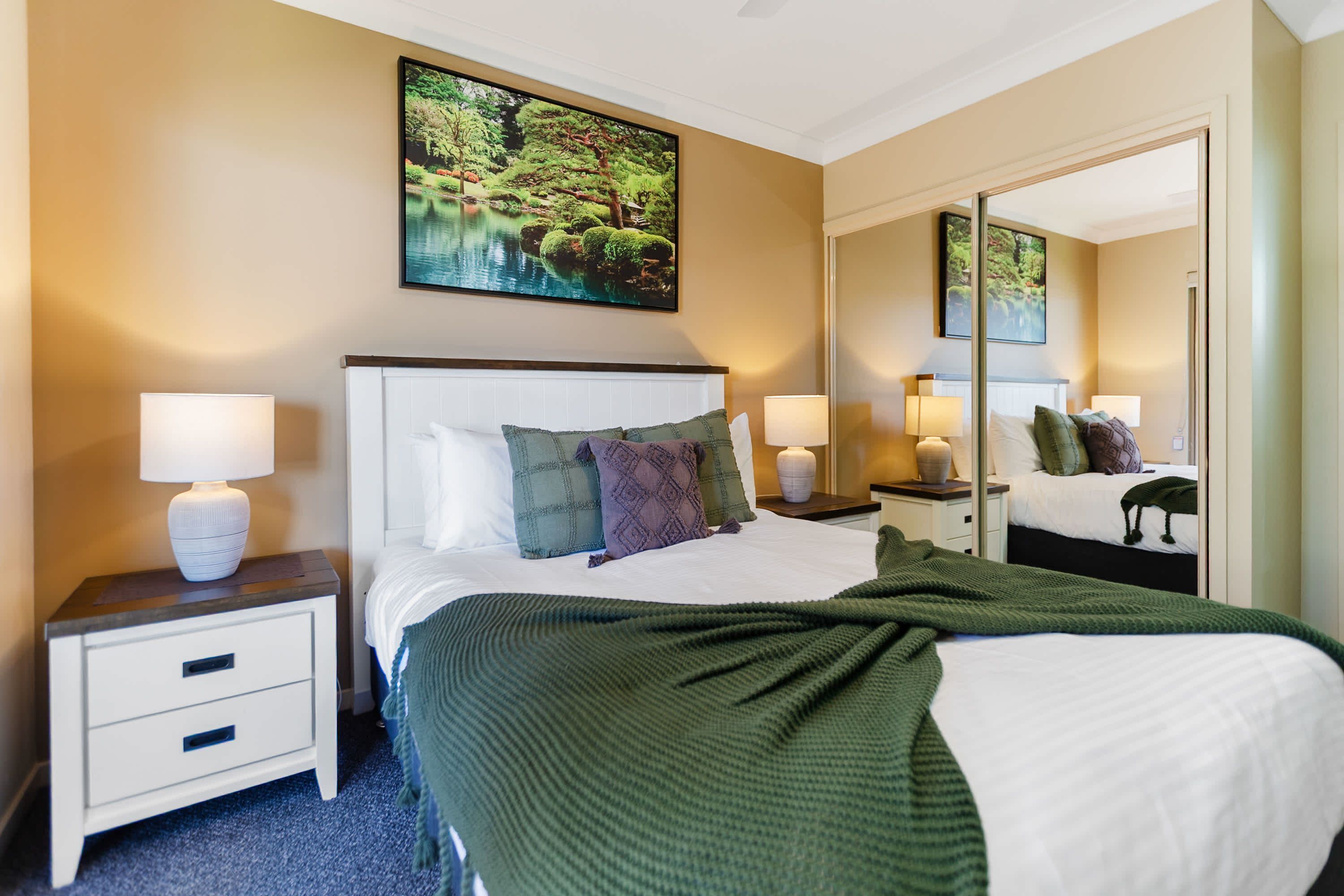 Une chambre d’hôtel avec un grand lit, deux tables de chevet avec des lampes, une commode et un grand miroir.