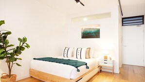 Un dormitorio moderno con una cama de madera, paredes blancas, una planta verde y un cuadro.
