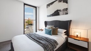 A modern bedroom with a large bed, a nightstand, a bedside table, a window, and a painting on the wall. - Chic 1-bed With a Sleek Balcony Near Shops (Melbourne)