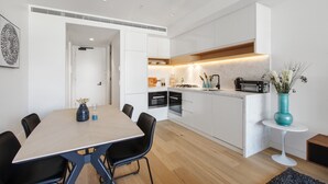 A modern kitchen with white cabinets, a wooden dining table, and black chairs. - Chic 1-bed With a Sleek Balcony Near Shops (Melbourne)