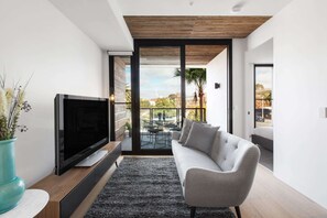A modern living room with a flat-screen TV, a grey sofa, and a large window overlooking a balcony with outdoor furniture. - Chic 1-bed With a Sleek Balcony Near Shops (Melbourne)