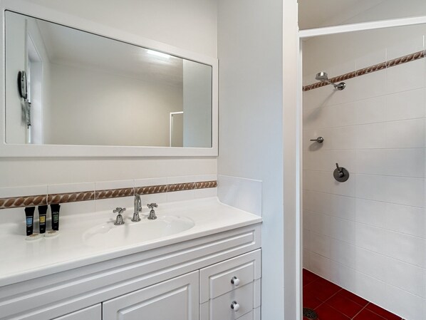 A bathroom with a white vanity, a large mirror, and a shower area with a towel rack. - Spacious 4-bed Home With Coastal Charm (Long Beach)