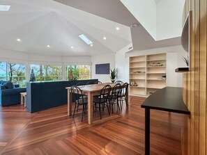 A modern living room with a wooden dining table, a sofa, and a built-in bookshelf. - Spacious 4-bed Home With Coastal Charm (Long Beach)