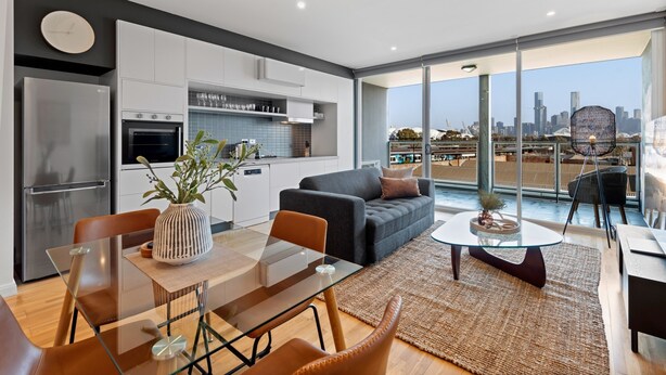 A modern apartment with a kitchen, dining area, and living room. It features a large balcony with a city view. - Modern 1-bed, City Skyline Views & Close to Shops (Melbourne)