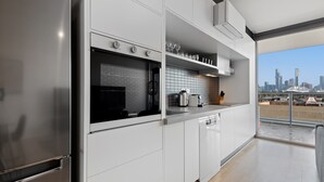 A modern kitchen with a stainless steel refrigerator, a built-in oven, and a dishwasher. There is a window with a city skyline view. - Modern 1-bed, City Skyline Views & Close to Shops (Melbourne)